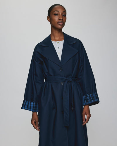 Aune Trench Coat i marineblå med rutete fôr, bred krage og belte i midjen for en elegant og tidløs stil.